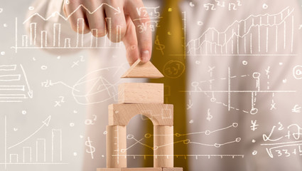 Young handsome businessman using wooden building blocks with white calculations scribbled around him