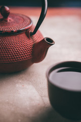 Traditional red asian iron teapot with clay cup full of green tea