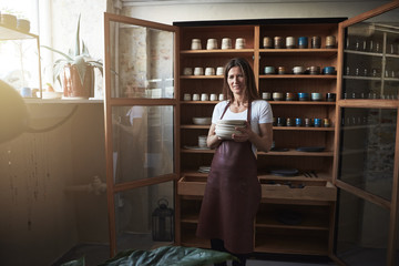 Smiling artisan standing with ceramic plates in her pottery studio