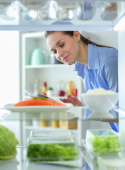 Portrait of female standing near open fridge full of healthy food, vegetables and fruits