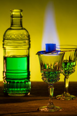 Bottle of absinthe and glasses with burning cube brown sugar.