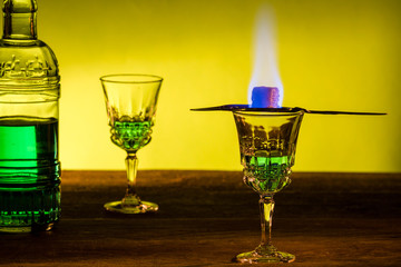 Bottle of absinthe and glasses with burning cube brown sugar.