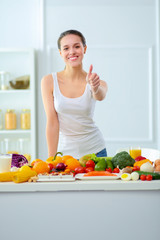 Young and cute woman sitting at the table full of fruits and vegetables in the wooden interior