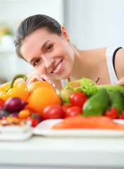 Young and cute woman sitting at the table full of fruits and vegetables in the wooden interior