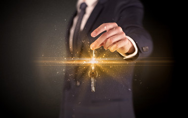 Businessman hand  over shiny keys in dark suit with dark background
