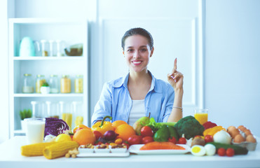 Young and cute woman sitting at the table full of fruits and vegetables in the wooden interior