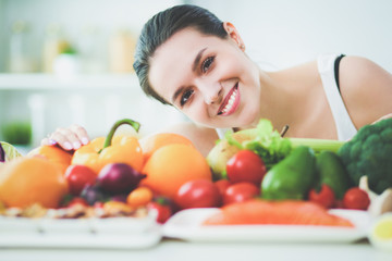 Young and cute woman sitting at the table full of fruits and vegetables in the wooden interior