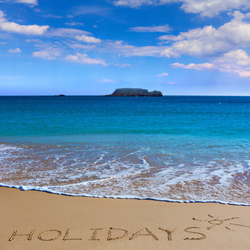 HOLIDAYS insctiption under the sun drawing on wet beach sand with the turquoisesea and the island on background