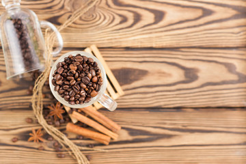 Lot of fried coffee beans in transparent glass for mulled wine on pallet near anise and threads and three cinnamon sticks and coffee beans poured out of glass on old wooden rustic brown table