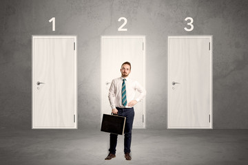 Fototapeta premium Businessman in grey room with three numbered white door behind his back 