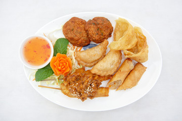 Mixture of Thai appertizers with deep-fried spring rolls, curry puffs, wontons, fish cakes and chicken satay skewers