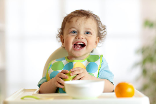 Cute baby child eating healthy food. Portrait of happy kid boy with bib in high chair.