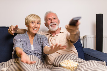 Senior couple lying on bed and watching TV together.