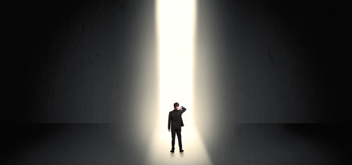 Businessman standing and seeing the light at the end of a big wall
