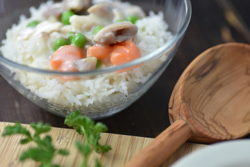Chicken fricassee with green pea served with boiled rice on a wooden background.
