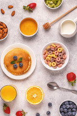 Breakfast with colorful cereal rings, pancakes, fruit, milk, juice.