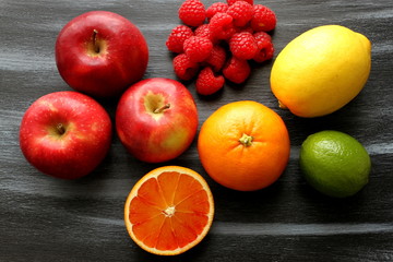 Apples, group of raspberries, lime, lemon and blood orange on shabby painted, black and blue board, top view