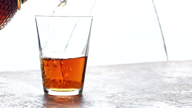 Pouring whiskey into a glass on old wooden table and light blurred background.