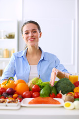 Young and cute woman sitting at the table full of fruits and vegetables in the wooden interior