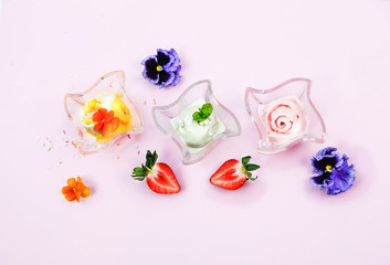 Ice cream in wave glass bowls and creamy milk beverage, smoothie with edible flowers *pansy, violet (on pink background. Pink (strawberry), yellow (mango or banana)  Top view