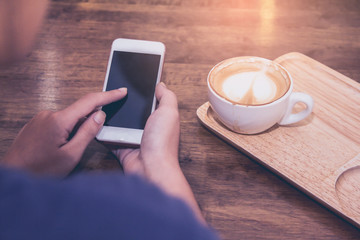 Close up of woman hands holding touching mobile phone with blank copy space for your text message in cafe with light Sunset,Vintage tone.Selective focus