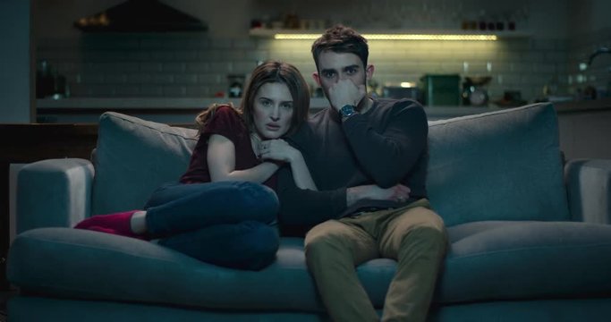 Frightened couple on a sofa late at night watching a scary horror film.