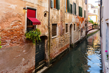 Typical tiny bridge on Venice canal. Flowers on windows with Venetian shutters