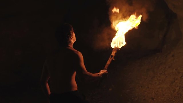 Careful hermit with burning torch in hand walks and looks around in stone cave