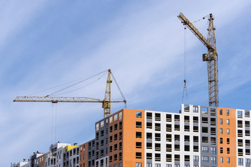 large yellow construction crane, multi-storey house against the blue sky