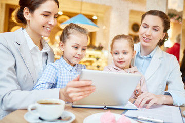 Two female employees and their daughters watching curious video in the net while spending time in cafe
