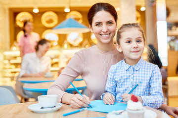 Young woman and her cute daughter drawing with crayons while spending time in cafe