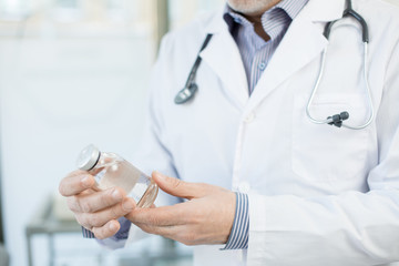 Clinician in whitecoat holding bottle with transparent liquid prepared for one of his patients