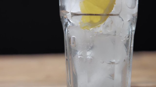 glass with ice and lemon slice on black background with homemade lemonade pouring in it