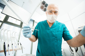 Gloved dentist or surgeon in mask, eyewear and uniform looking at patient before oral check-up