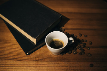 A cup of black coffee and coffee beans and a book on a wooden table. top view.