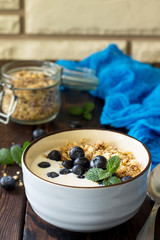 Homemade healthy breakfast in a bowl with homemade baked granola, fresh blueberries and yogurt on the kitchen wooden rustic table. Copy space.