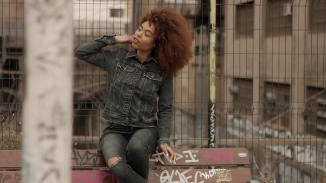 black mixed race woman with big afro curly hair sits on bench with graffity