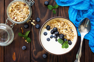 Homemade healthy breakfast in a bowl with homemade baked granola, fresh blueberries and yogurt on the kitchen wooden rustic table. Top view flat lay background.