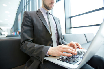 Contemporary agent with laptop on knees browsing in the net while waiting for his flight