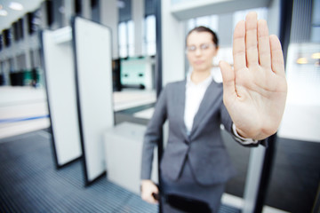 Hand of female security showing stop gesture to someone while standing by gates in airport entrance