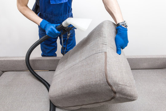 Cleaning Service. Man Janitor In Gloves And Uniform Vacuum Clean Sofa With Professional Equipment