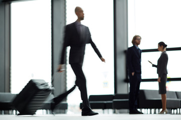 Blurry human figure moving along airport lounge with suitcase and hurrying for flight