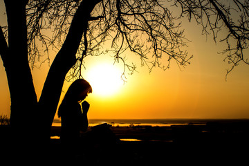 silhouette of woman praying to God in the nature witth the Bible at sunset, the concept of religion...
