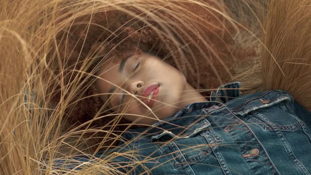 mixed race woman with huge curly hair lying down on lawn with high dry grass