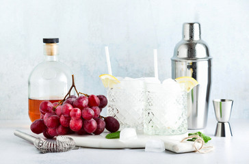 Bar accessories for mixing cocktails and fresh ripe grapes. A bottle of alcohol and two glasses of ice