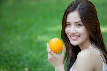 Portrait of pretty girl holding orange fruit at summer green park.