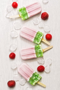 Pink green ice cream on a stick on a white wooden background. Strawberry and kiwi ice cream.