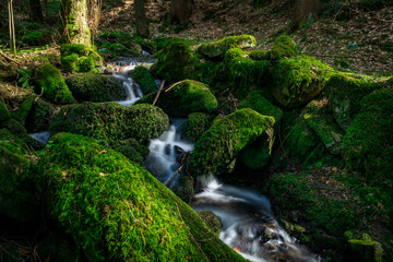 Bachlauf mit Steinen und Moos mit Wasserfall im Bayerischen Wald