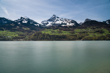 beautiful turquoise mountain lake panorama with snow-covered peaks and green meadows and forests