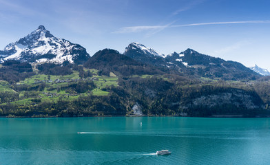 beautiful turquoise mountain lake panorama with snow-covered peaks and green meadows and forests and boats  on the lake